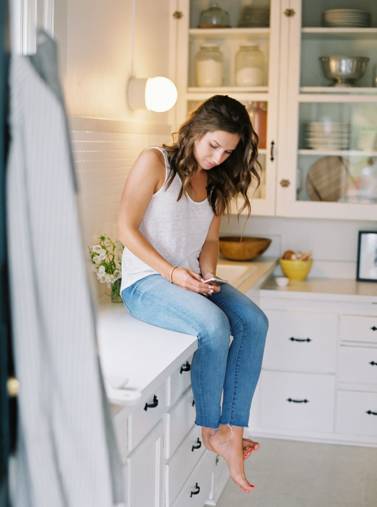 Woman sitting on kitchen counter using smartphone casually