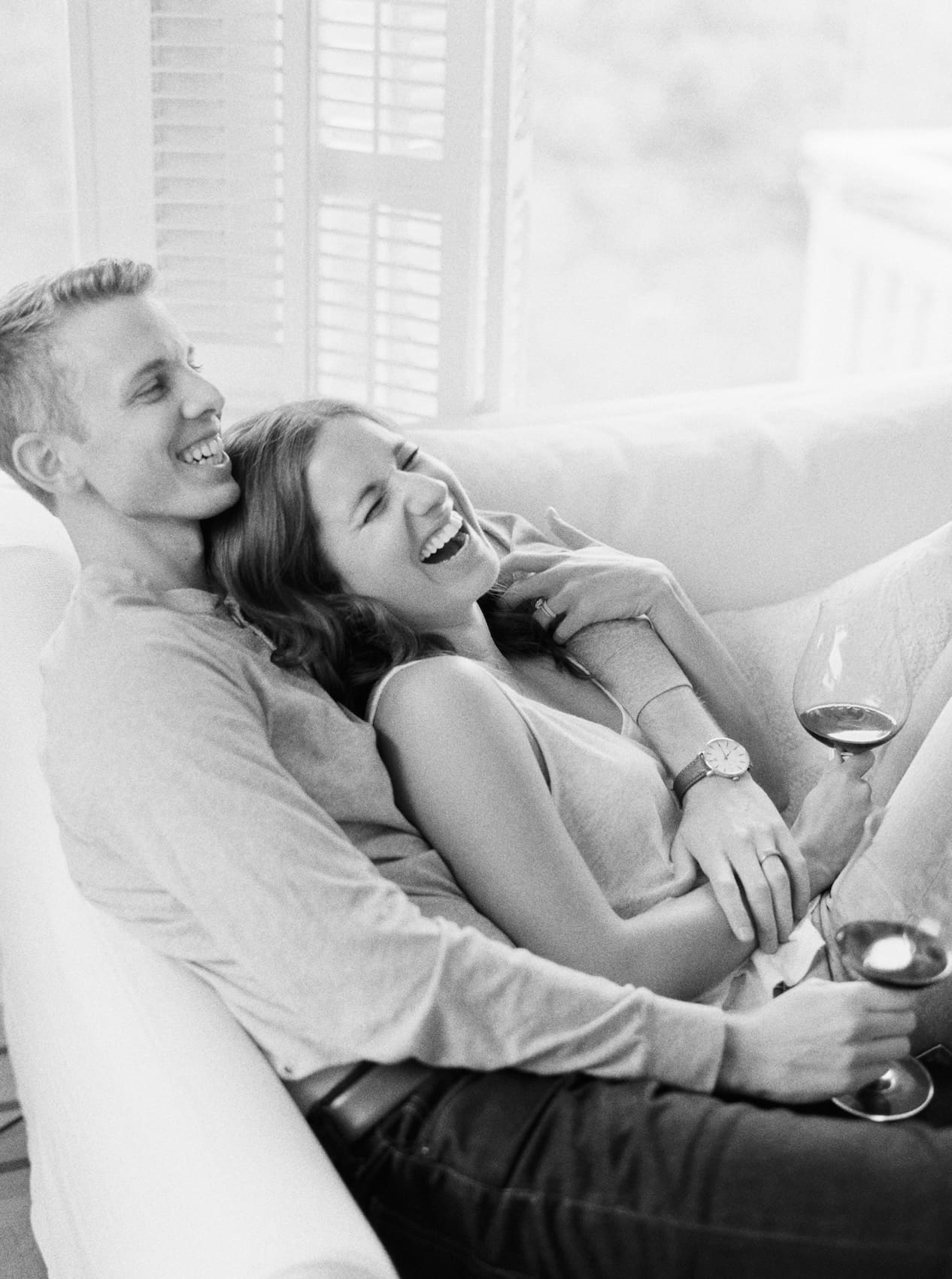 Couple laughing together on a couch holding glasses of wine