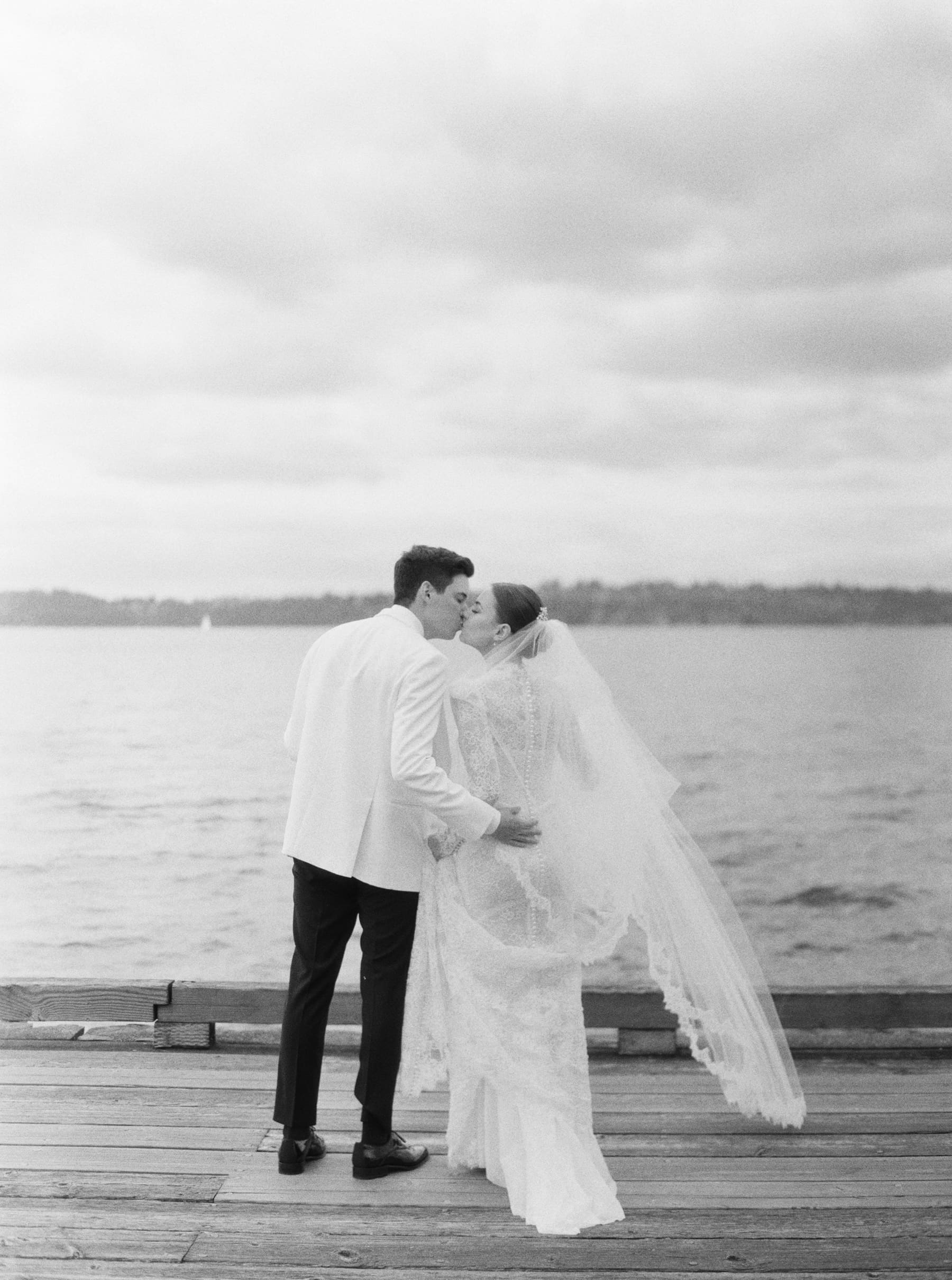 black and white film photo of bride and groom kissing on the woodmark hotel dock at their wedding 